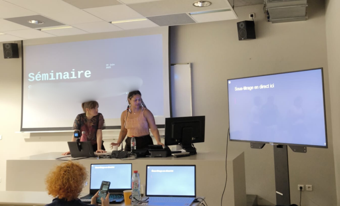 Deux jeunes femmes présentent un séminaire, à côté d'elles se trouve un écran de sous-titrage