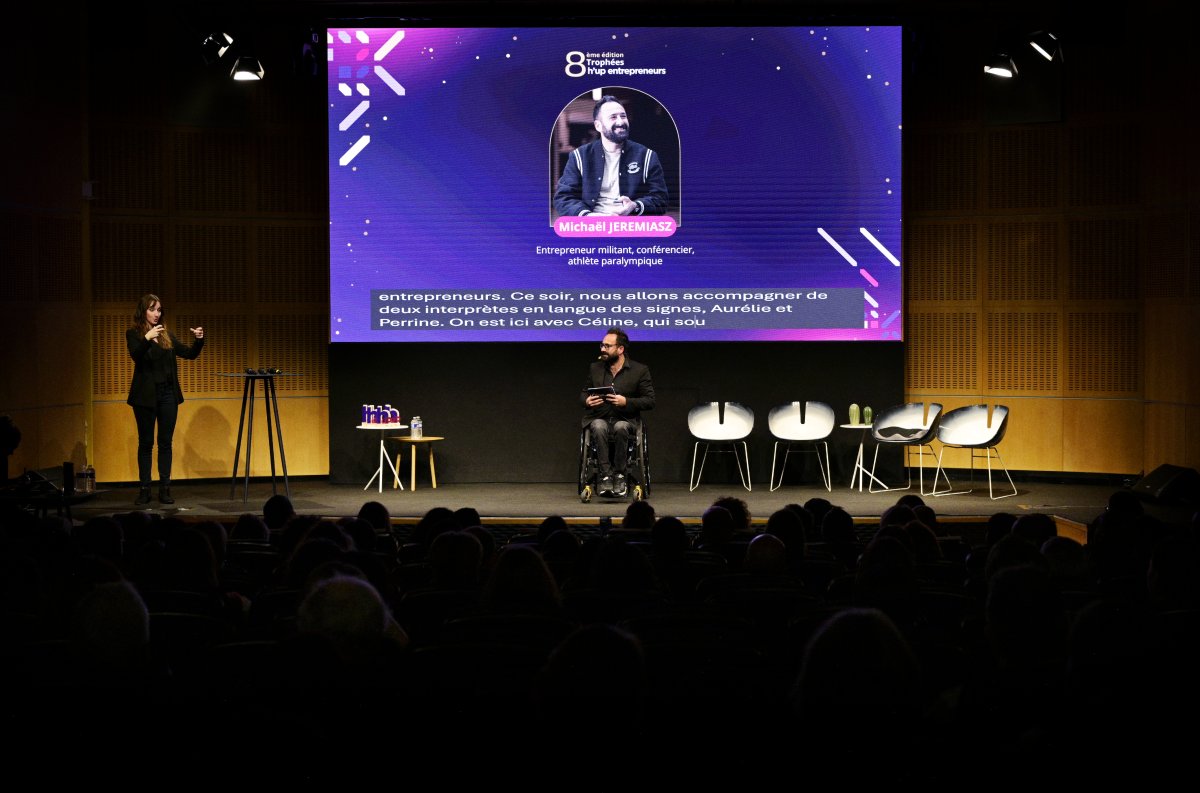 Dans une grande salle de conférences, un petit écran retransmet le sous-titrage