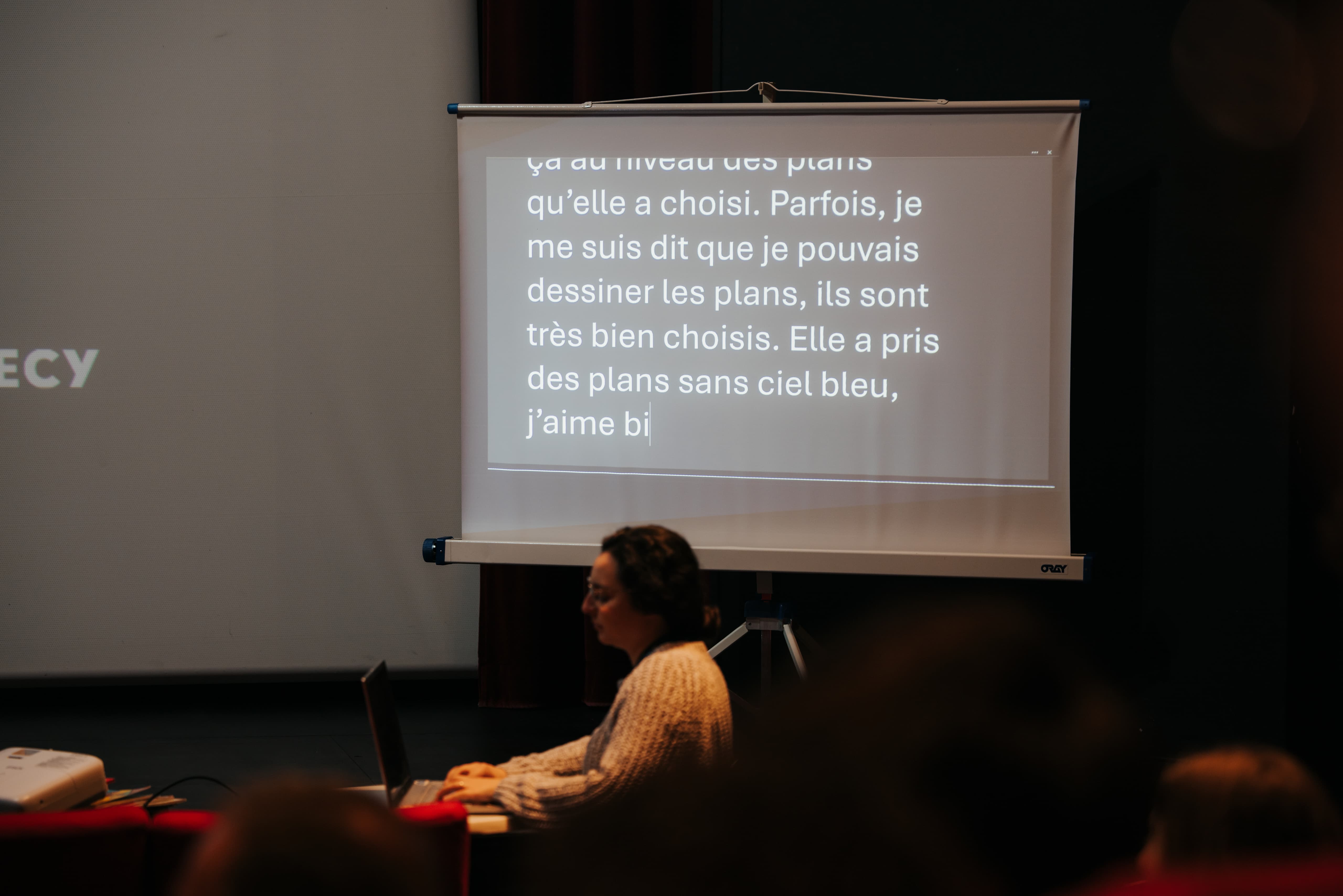 Céline tape à l'ordinateur tandis qu'un texte s'affiche sur un grand écran