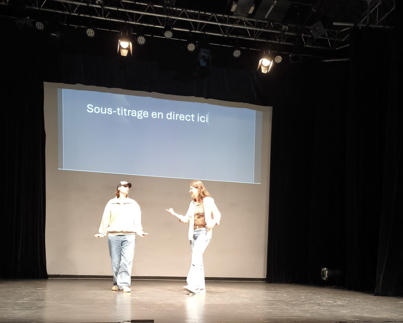 Deux actrices jouent sur scène devant un écran de surtitrage