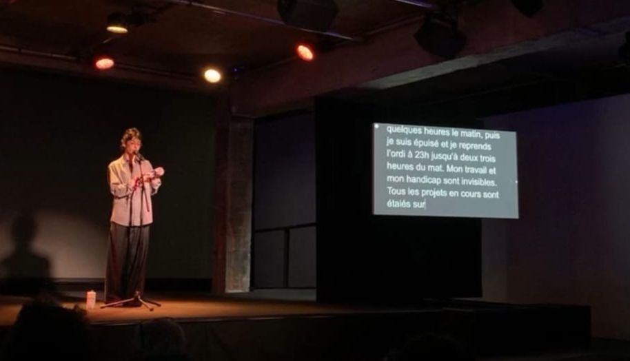 un artiste lit un texte, près de lui, un écran retransmet le sous-titrage